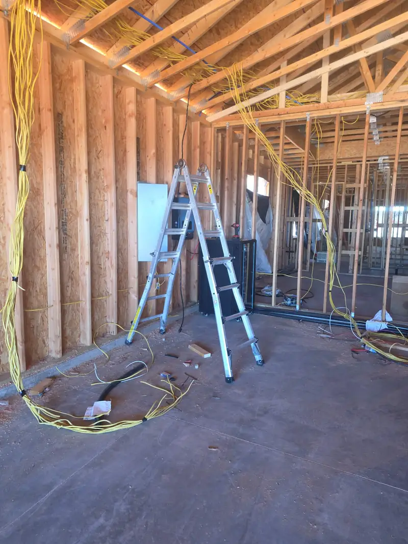 Electrical rough-in inside a house under construction, with yellow cable runs stapled through open wall studs and roof trusses.