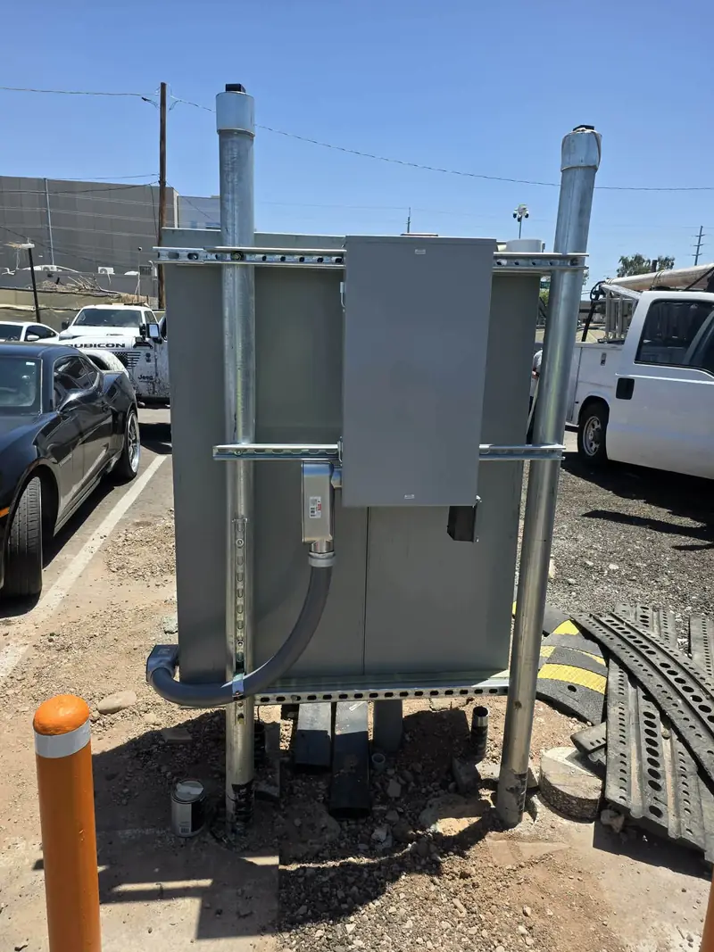 Outdoor electrical equipment installation: a grey enclosure with rigid conduit risers and a disconnect mounted alongside.
